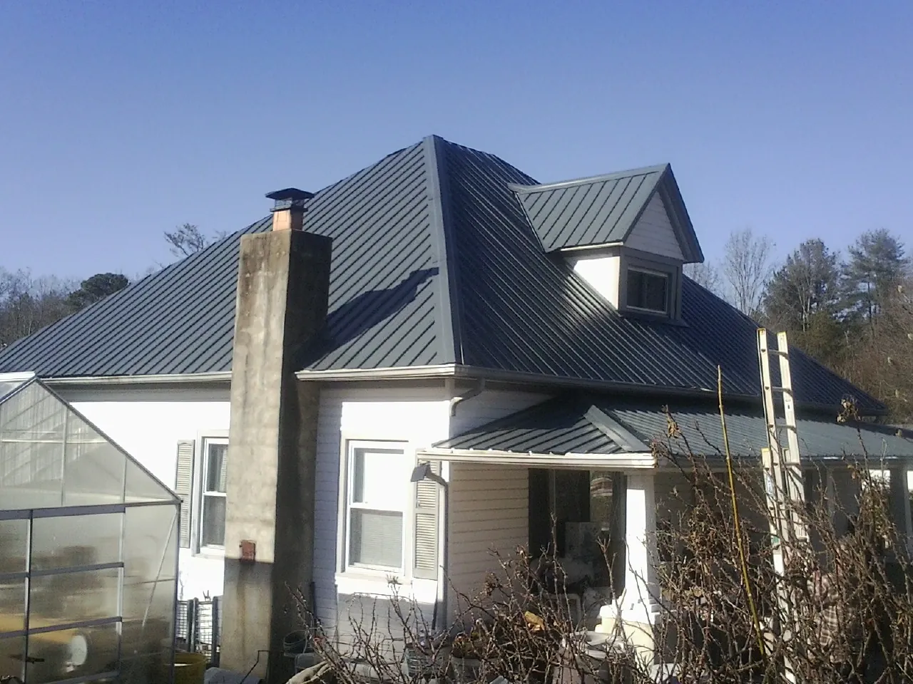 Dark blue standing seam metal roof on a white farmhouse with dormer — Slate & Tile Roof Repair by Roofing Brothers in Castaic