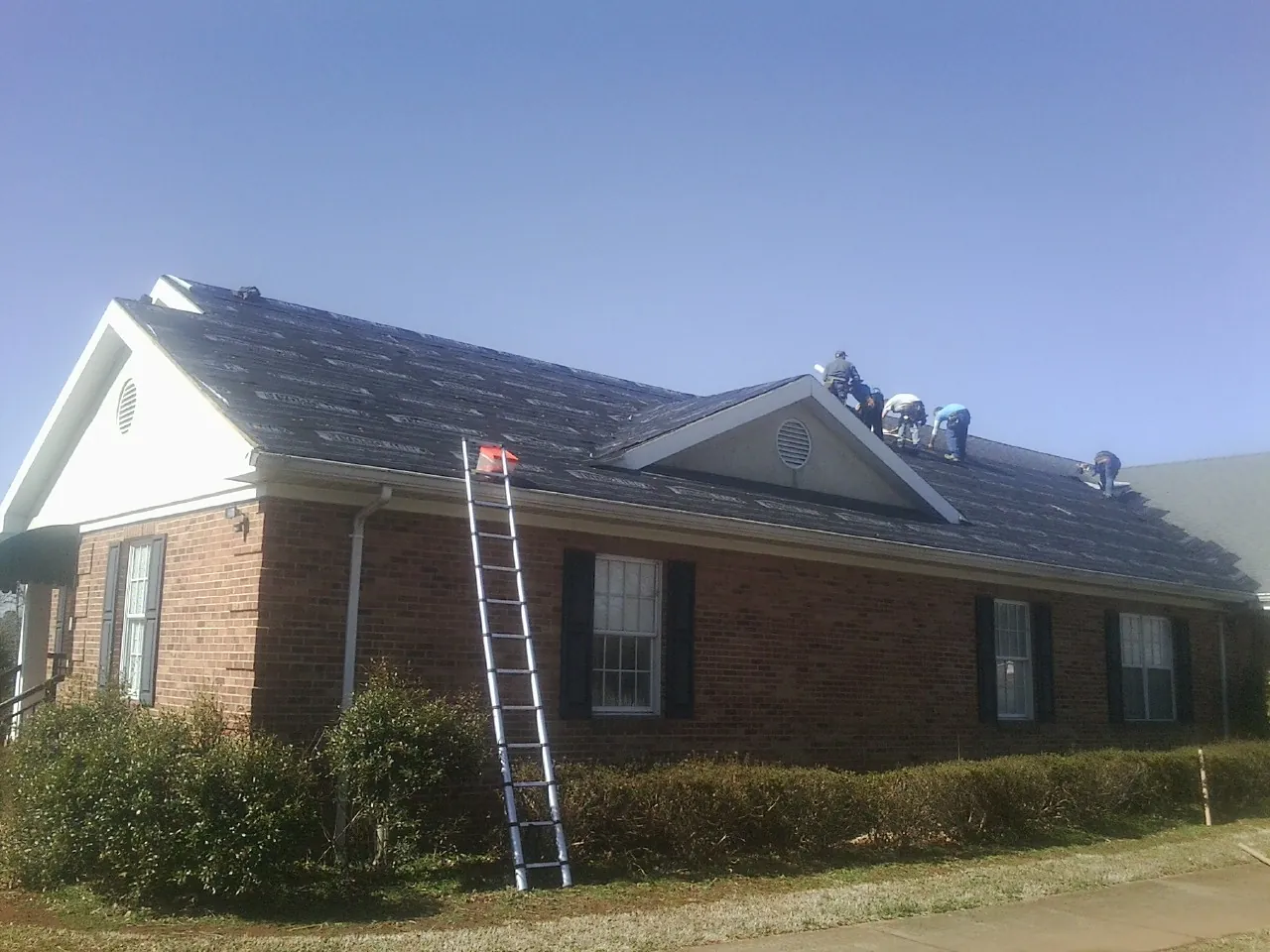 Crew tearing shingles off a brick ranch roof with a ladder set — Metal Roof Repair work by our crew in Castaic