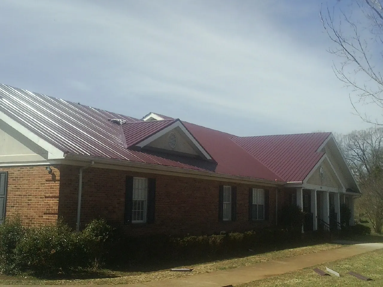 Red metal roof with gabled entries on a long brick building, from a Hail Damage Roof Repair job in Castaic