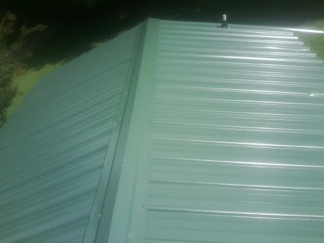 New green metal panels meeting at the ridge of a roof — Flat Roof Repair work by our crew in Castaic