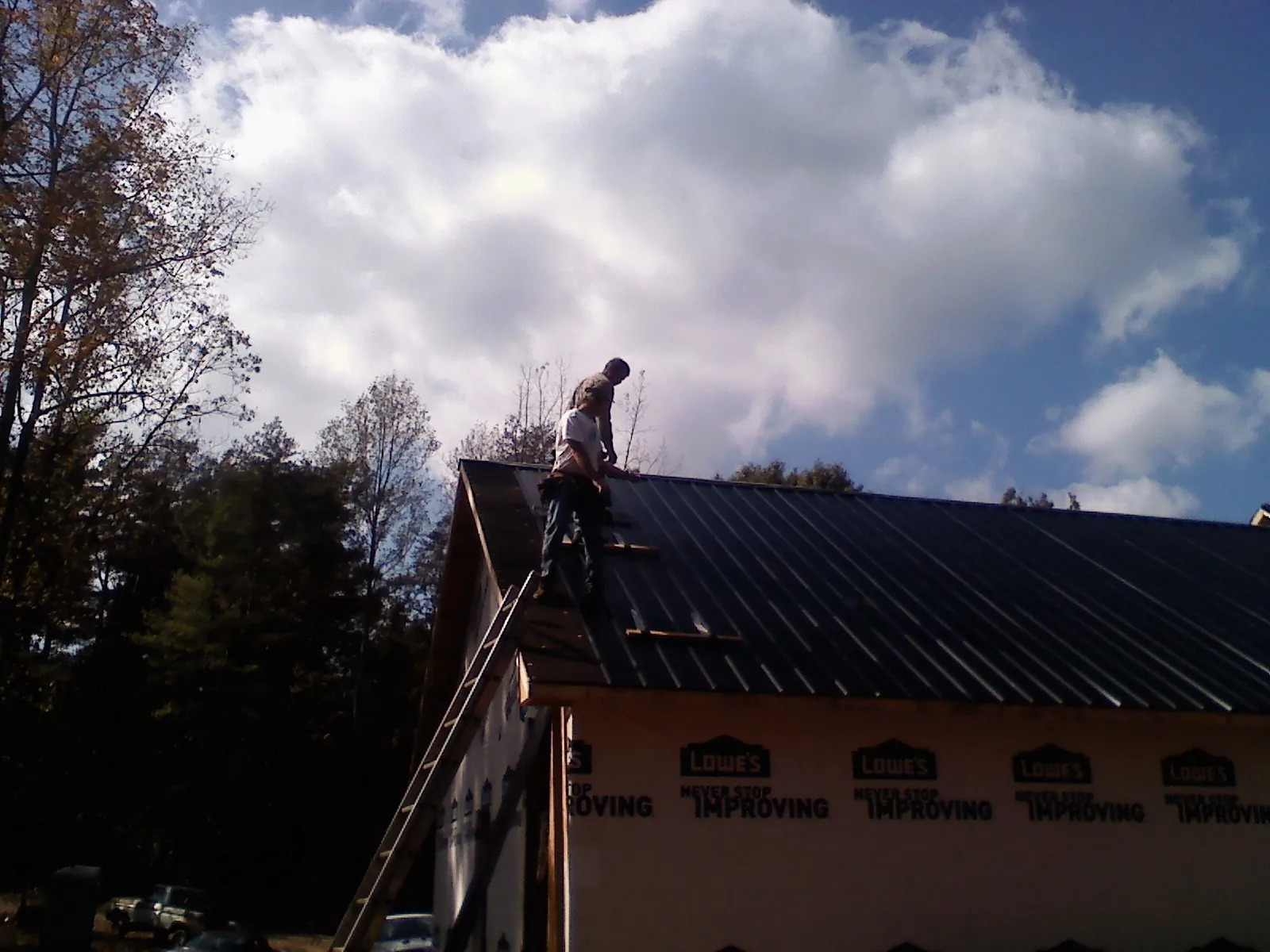 Roofer fastening dark metal panels high against a cloudy sky, from a Roof Inspection job in Castaic