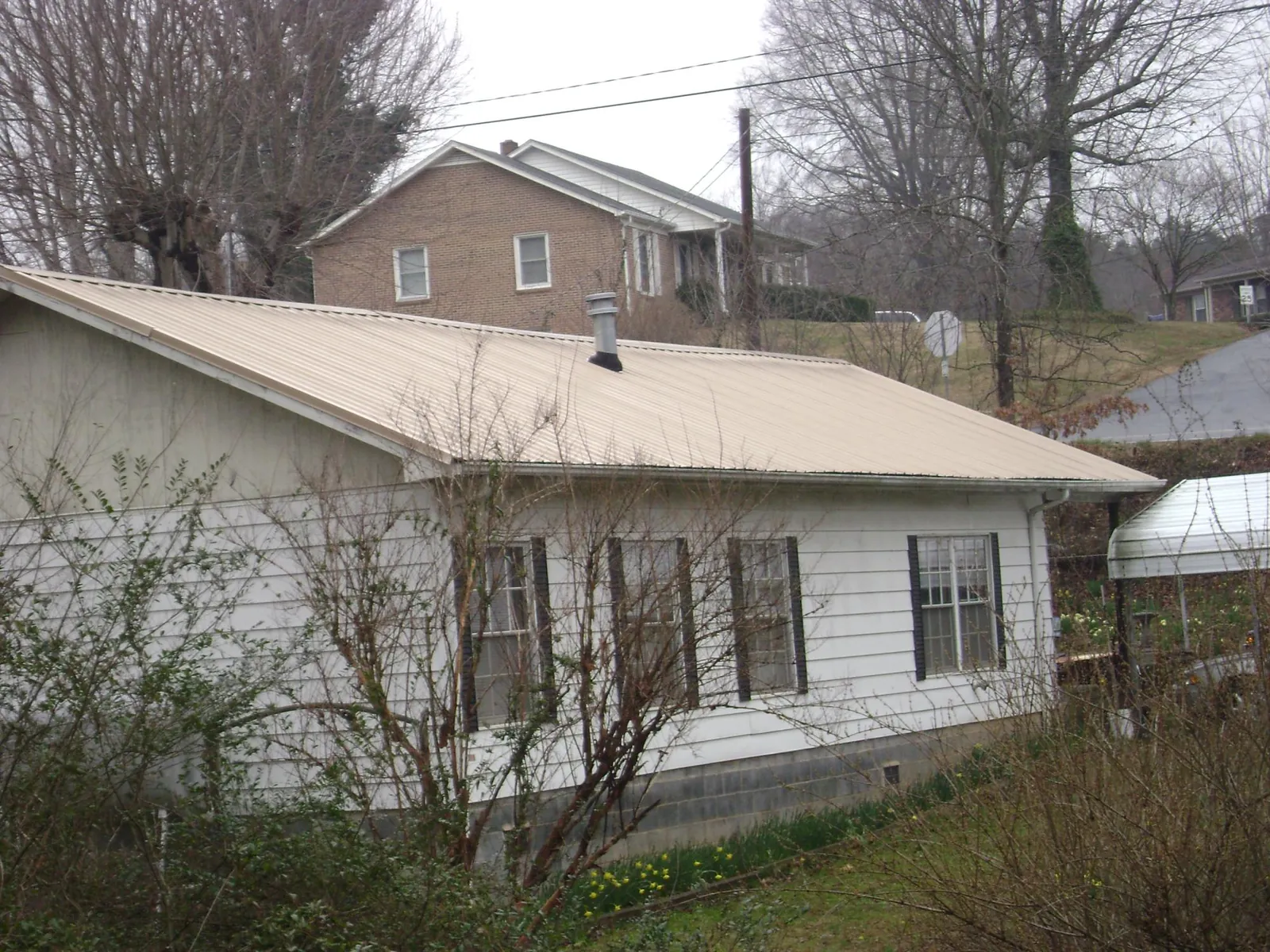 Tan metal roof on a white sided house set into a hillside — Commercial Roofing by Roofing Brothers in Castaic